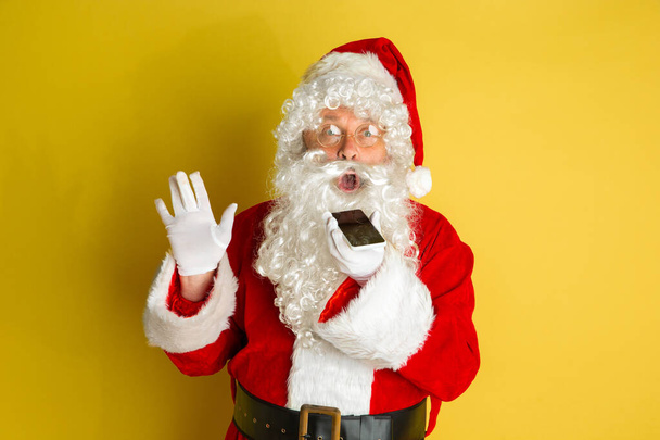 Santa Claus with modern gadgets isolated on yellow studio background - Foto, Bild