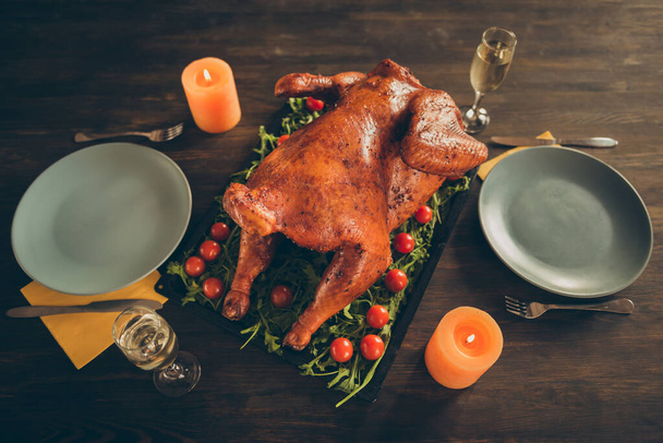 Top above high angle photo of big tasty roast chicken on tray with red cherry tomato herbs served table for two people couple celebrate thanksgiving have plates knifes forks candles glass isolated - Fotó, kép