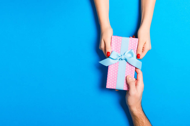 Bovenaanzicht van een cadeau in mannelijke en vrouwelijke handen op kleurrijke backg - Foto, afbeelding