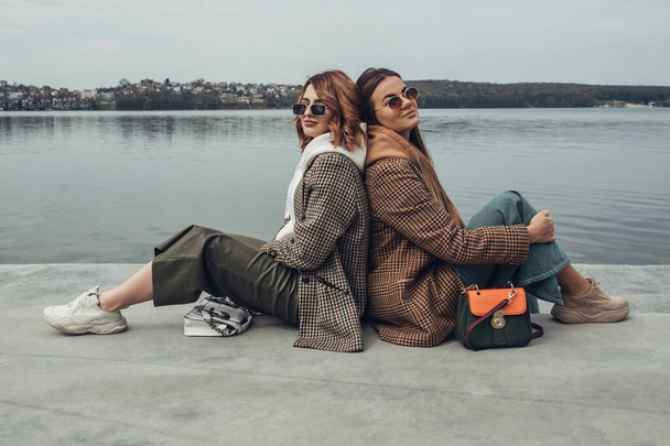 Kahden muodin tyttöjen muotokuva, parhaat ystävät ulkona, tyylikäs takki, kävely lähellä järveä
 - Valokuva, kuva