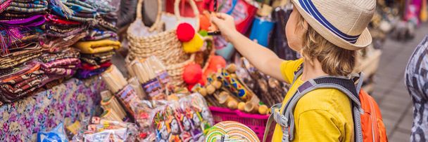 BANNER, LARGO FORMATO Niño en un mercado en Ubud, Bali. Tienda de souvenirs típica que vende souvenirs y artesanías de Bali en el famoso Mercado de Ubud, Indonesia. Mercado balinés. Recuerdos de madera y artesanía
 - Foto, Imagen
