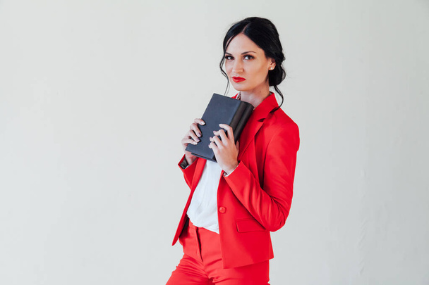 портрет красивой брюнетки с книгой в красном деловом костюме в офисе
 - Фото, изображение
