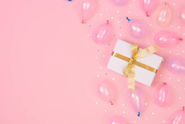 Композиція подарункової коробки з прикрасами та повітряною кулею, конфетті на рожевому пастельному тлі. день народження, новорічна концепція. Плоский простір, вид зверху, простір для копіювання
. - Фото, зображення
