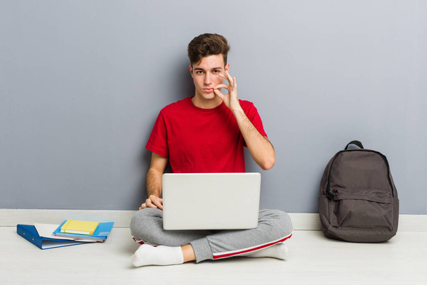 Jeune homme étudiant assis sur le sol de sa maison tenant un ordinateur portable
 - Photo, image