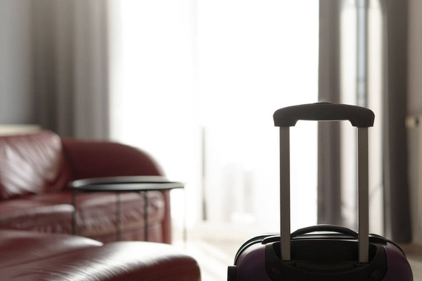 A suitcase standing by the window in the living room near a leather red sofa - Foto, Bild