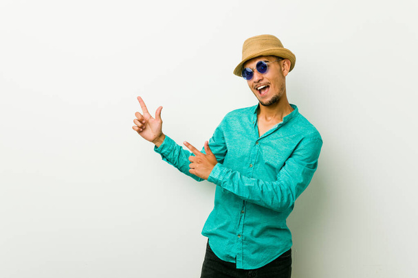 Young hispanic man wearing a summer clothes pointing with forefingers to a copy space, expressing excitement and desire. - Foto, Bild