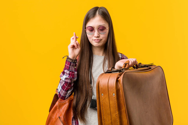 Young asian woman holding a suitcase crossing fingers for having luck - 写真・画像