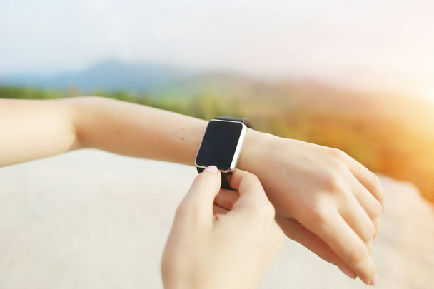 Sunny photo of closeup hands using smartwatch with mountains in background. - Foto, Imagem
