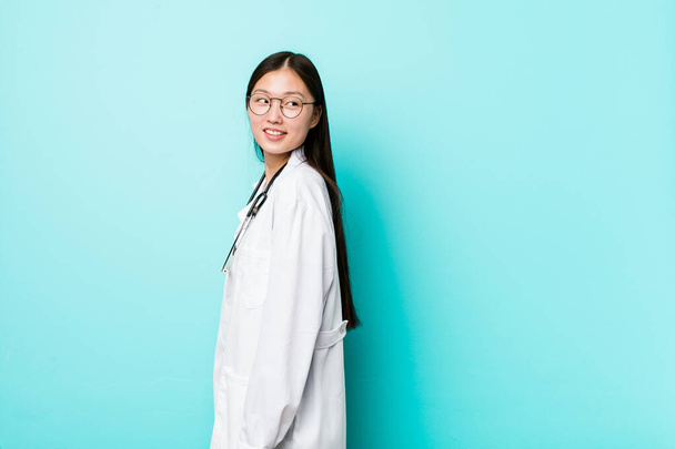 Jeune femme médecin chinois regarde de côté souriant, gai et agréable
. - Photo, image