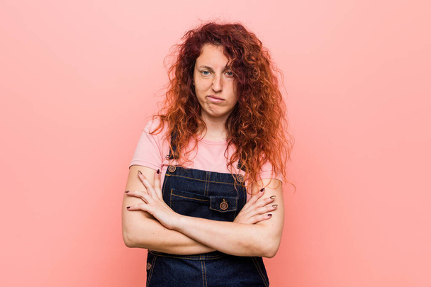 Young pretty ginger redhead woman wearing a jeans dungaree unhappy looking in camera with sarcastic expression. - Photo, Image