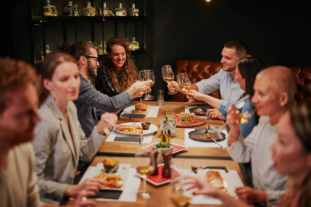 Grupa najlepszych przyjaciół siedzi w restauracji, jedząc kolację, pijąc wino i bawiąc się. - Zdjęcie, obraz