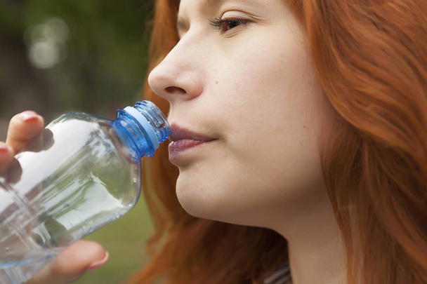 čistá pitná voda, mladá zrzavá dívka s lahví vody, balená voda - Fotografie, Obrázek