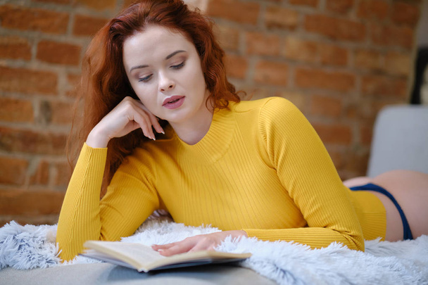 Red-haired woman reads a book at home - Fotografie, Obrázek