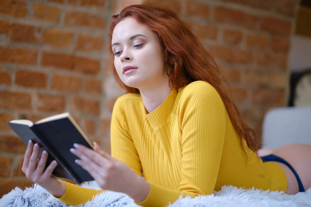 Red-haired woman reads a book at home - Foto, imagen