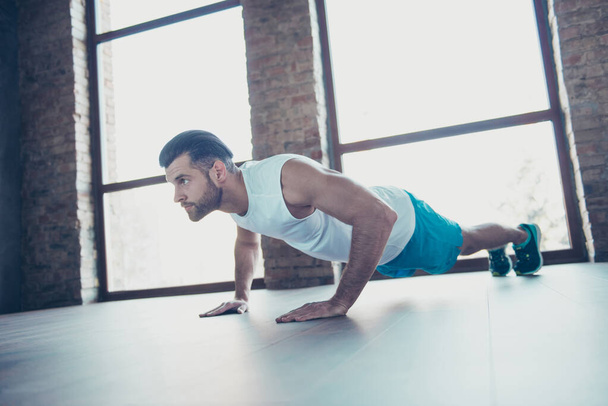 Profile photo of macho sportsman guy do push ups plank hands leaning floor determined trainer sportswear tank-top shorts sneakers training house studio windows indoors - Photo, Image