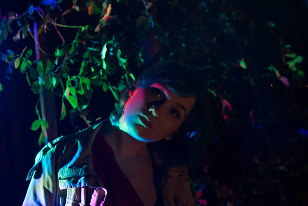 Jeune femme dans le jardin illuminée par la lumière multicolore
. - Photo, image