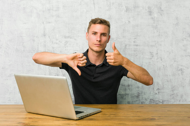 Молодий підприємець, який працює зі своїм ноутбуком на столі, показує великі пальці вгору і великі пальці вниз, складна концепція вибору
 - Фото, зображення