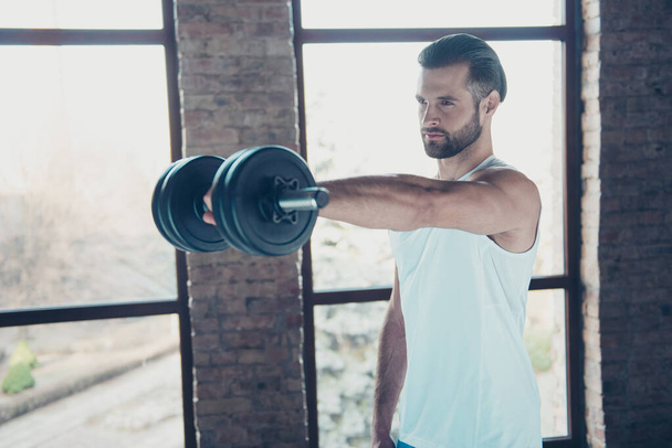 Profile photo of handsome hot beard guy morning training biceps muscles lift heavy dumbbell tempting eyes look sportswear tank-top training house studio big windows indoors - Foto, immagini
