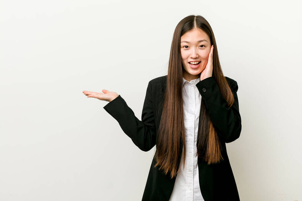 Μια νεαρή, όμορφη Κινέζα επιχειρηματίας κρατάει φωτοτυπίες σε μια παλάμη, κρατώντας το χέρι πάνω από το μάγουλο. Έκπληκτη και χαρούμενη. - Φωτογραφία, εικόνα