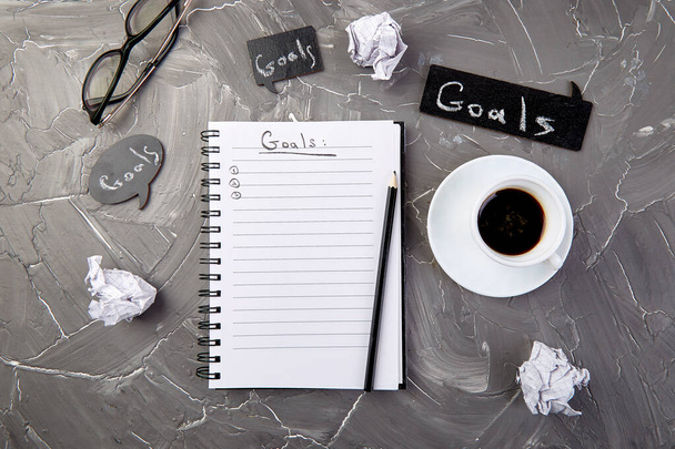 Ziele als Notiz auf Notizbuch mit Idee, zerknülltes Papier, Tasse Kaffee auf grauem Hintergrund. Ansicht von oben. - Foto, Bild