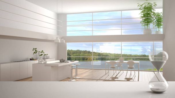 Biały stół lub półka z kryształową klepsydrą mierzącą czas przelotu nad minimalistyczną białą kuchnią z wyspą, panoramiczne okno, architektura wnętrz, przestrzeń kopiująca tło - Zdjęcie, obraz