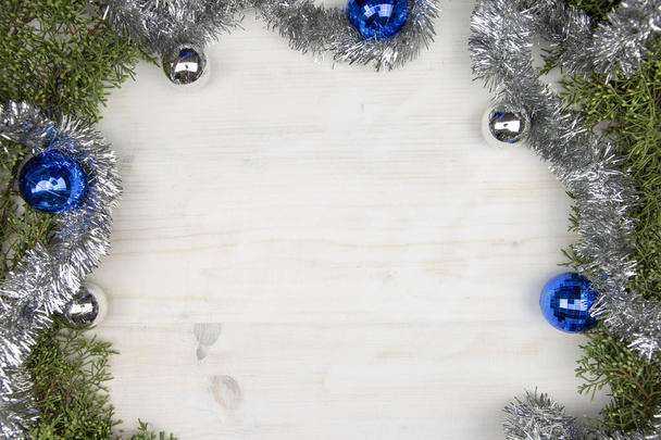 Christmas space with pine branches, silver garland and silver and blue Christmas baubles on a light wooden background - Foto, Imagem
