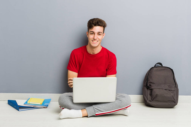 Young student man sitting on his house floor holding a laptop - Photo, Image