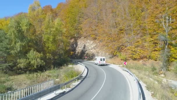 Biały Van, ciężarówka transportowa jadąca krętą górską drogą w słoneczny dzień. Złoty las po stronie drogi - Materiał filmowy, wideo