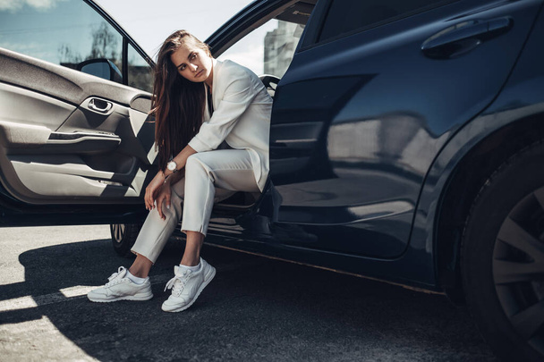 Moda menina elegante em terno branco posando perto do carro azul
 - Foto, Imagem
