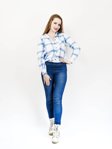 Beautiful happy woman posing white holding a collar of blue plaid shirt in jeans. Full body length standing over light background. - Foto, afbeelding