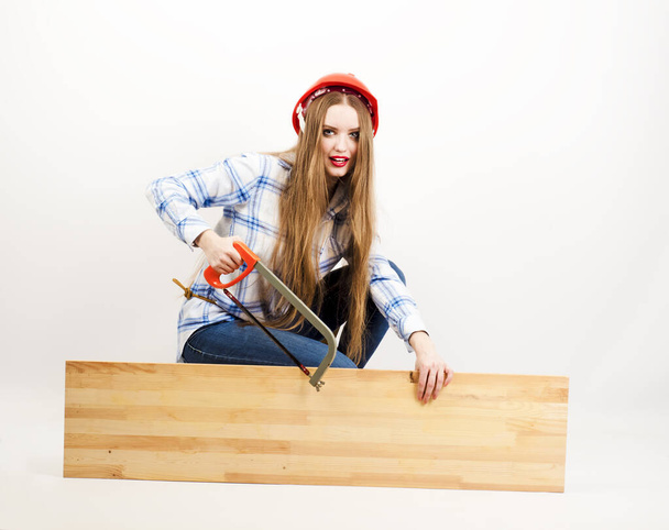 Portrait of a happy attractive attractive industrious young age professional female carpenter worker, sawing a wooden board on a light background - Photo, image