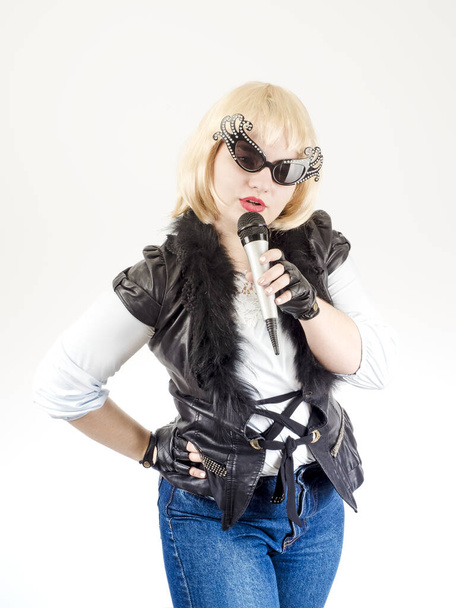 A semi-long portrait of a female rock musician in a black leather jacket and gloves on a gray background. The concept of music and rock style - Фото, изображение