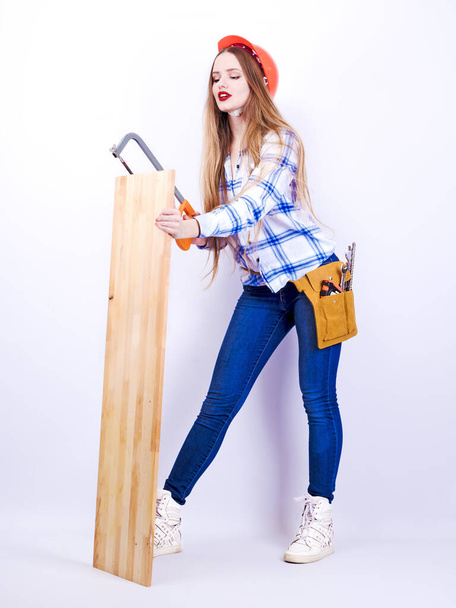 Portrait of a happy attractive attractive industrious young age professional female carpenter worker, sawing a wooden board on a light background - Φωτογραφία, εικόνα