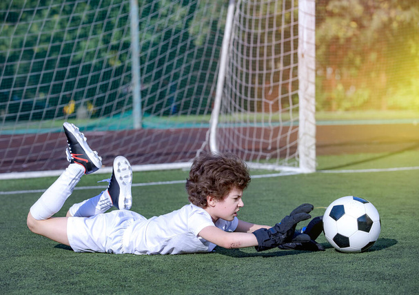 Young soccer goalie attempting to make a save. little soccer goalkeeper with gloves. Kids - soccer champion. Boy goalkeeper in football sportswear on stadium with ball. Sport concept. - Fotoğraf, Görsel