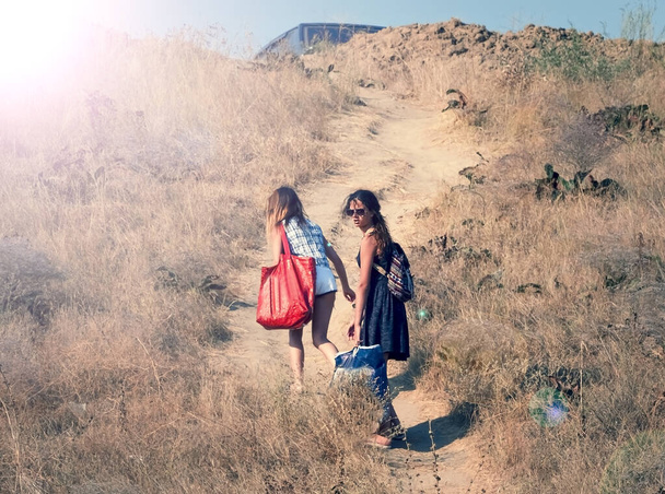 Two girls with heavy bags climb to the top of the hill. People walking from the beach to the car park on a hot summer day on the sea coast. Overcoming difficulties concept. - Fotoğraf, Görsel