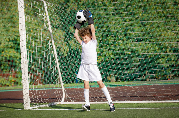 Summer soccer tournament for young kids. football club. emotions and joy of the game. Young goalie. Boy goalkeeper in football sportswear on stadium with ball. Sport concept. selective focus - 写真・画像