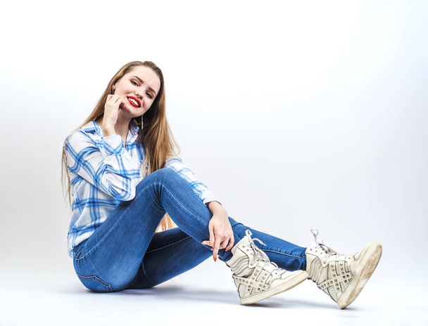 Beautiful young fashion model girl in blue jeans sitting on the floor on a white background. Natural beauty girls, teen and adolescent issues. - Valokuva, kuva