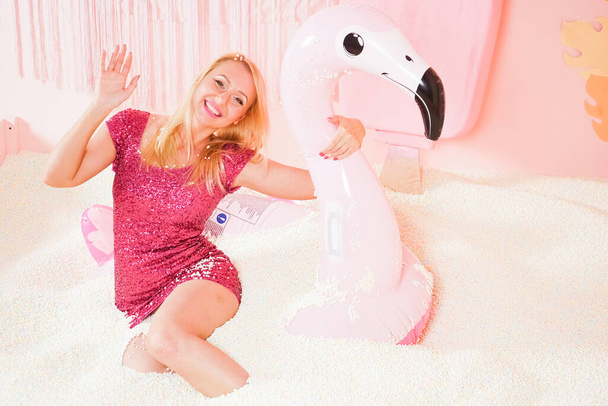 cute pretty woman in tight glitter summer dresswith inflatable flamingo in swimming pool with foam plastic balls - Photo, Image