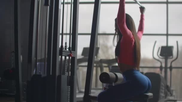 Una donna scuote la schiena durante un allenamento in palestra. Formazione in una stanza con grandi finestre sullo sfondo una donna utilizza un ellissoide e un tapis roulant
 - Filmati, video