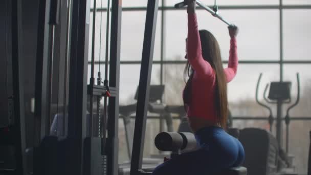 A rapariga sacode as costas num treino no ginásio. Treinamento em uma sala com grandes janelas no fundo uma mulher usa um elipsoide e uma esteira
 - Filmagem, Vídeo