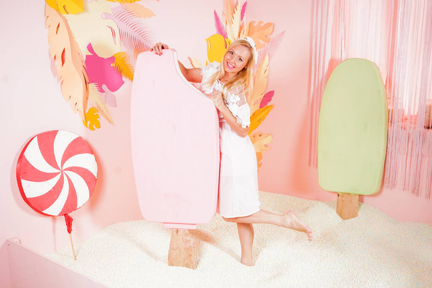 czarująca szczęśliwa blondynka w miękkiej koronkowej letniej sukience pozująca z ogromnymi różowymi lodami w basenie z pianką miękkie małe kulki i zaangażowana w terapię relaksacyjną. - Zdjęcie, obraz