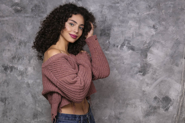 Beautiful woman with with light make up and curly hairstyle wearing distressed crop top sweater. - Foto, Imagem