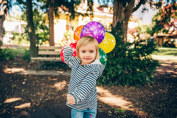 Funny kid girl playing with colorful balloons on playground - Фото, изображение