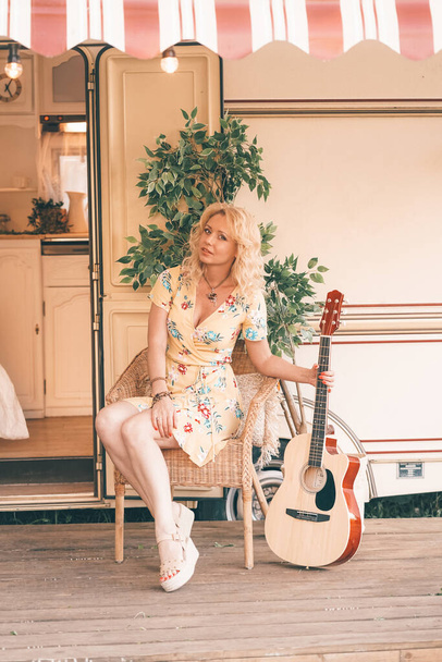 Loving middle age girlfriend with long blonde hair plays the guitar and singing song near camper van trailer - Photo, image