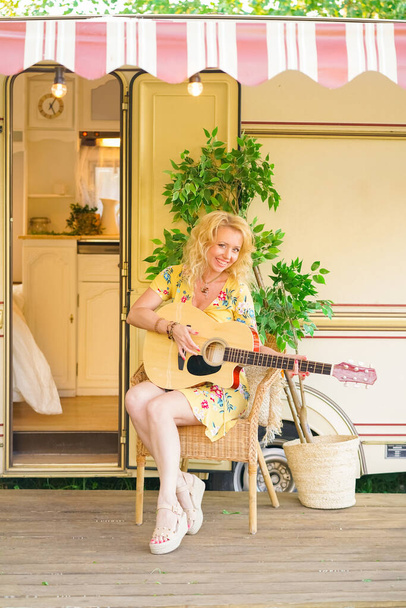 Amante de meia-idade namorada com longo cabelo loiro toca a guitarra e canção cantando perto trailer van campista
 - Foto, Imagem