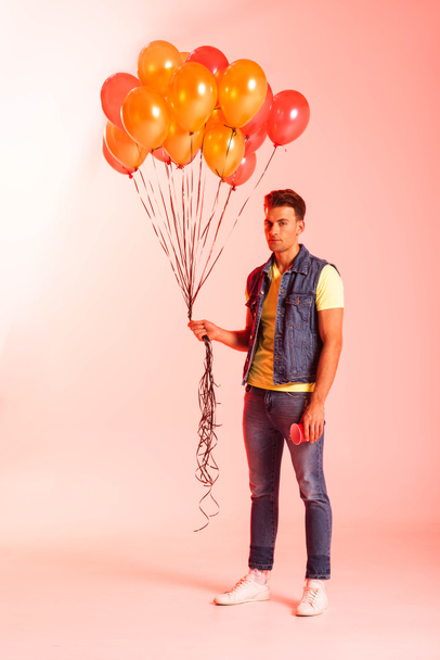 όμορφος άντρας κρατά πορτοκαλί μπαλόνια σε ροζ  - Φωτογραφία, εικόνα