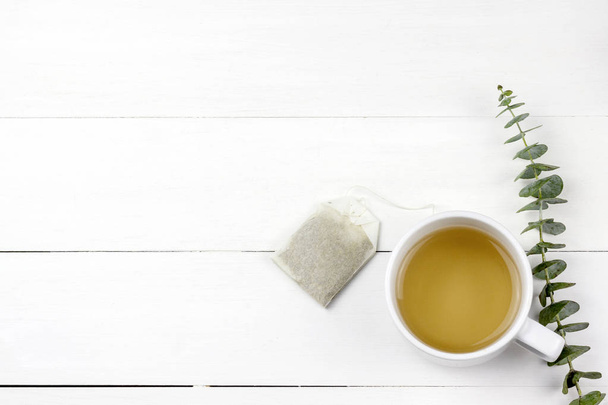Утренняя чашка чая с листьями эвкалипта Серебряный доллар на фоне панели белого дерева
 - Фото, изображение