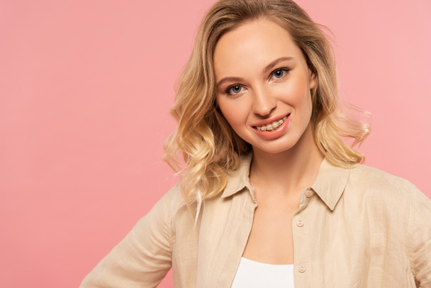 Blonde woman with dental braces smiling at camera isolated on pink - Фото, зображення