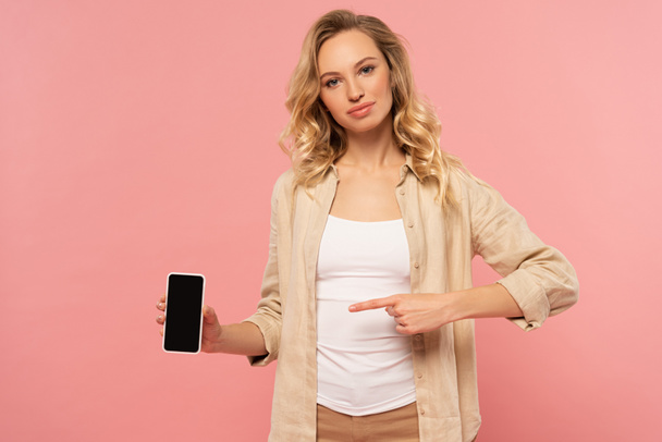 Woman pointing with finger on smartphone with blank screen isolated on pink - Фото, изображение