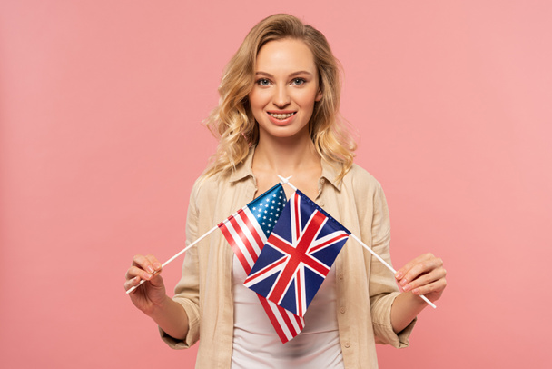 Gülümseyen sarışın kadın pembe üzerinde Amerikan ve İngiliz bayrakları taşıyor. - Fotoğraf, Görsel